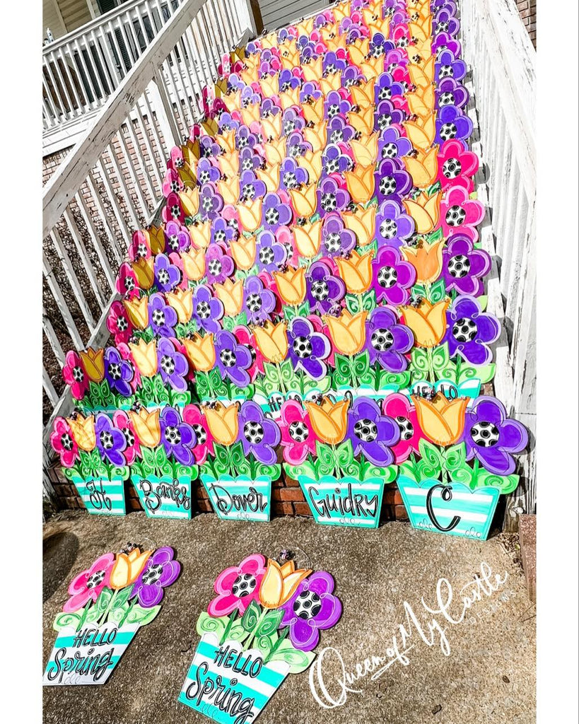 Door hangers in the shape of flower pots with blooming flowers. The door hangers are either personalized with the customer's last name or feature the text "hello spring."
